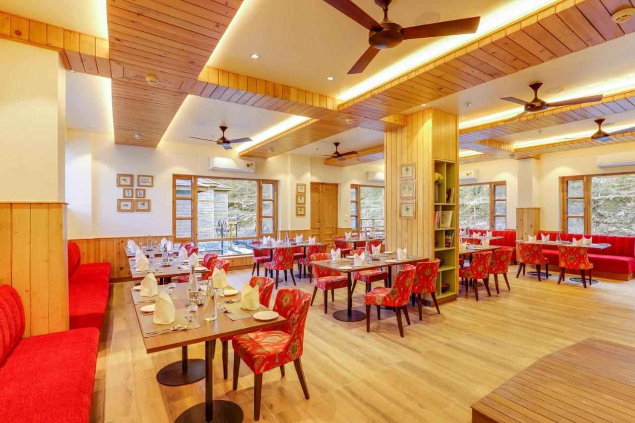 Un comedor amplio con varias mesas y sillas, ventiladores de techo y ventanas grandes.