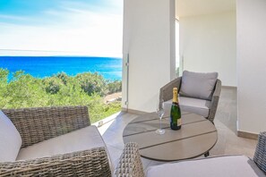 Un balcon agrémenté de meubles en osier, une table avec une bouteille et un verre, et une vue sur l’océan.