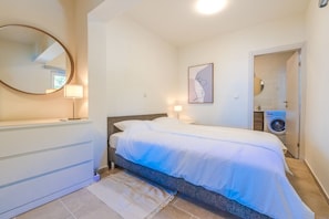 A bedroom with a bed, bedside lamps, a mirror, a wall-mounted artwork, and a washing machine in the adjacent room. - Villa Pietra Pag - Three Bedroom Villa, Sleeps 6 (Mulobedanj)