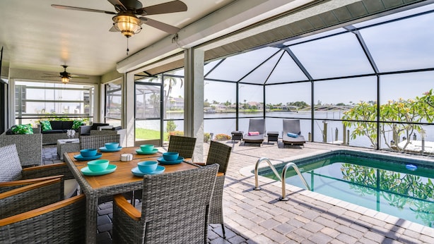 A covered outdoor area with a pool, wicker furniture, and a view of the lake. - Waterfront Cape Coral Home w/ Pool & Gulf Access (Cape Coral)
