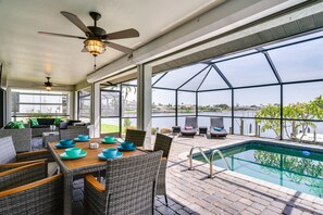 Un espacio al aire libre techado con piscina, mobiliario de mimbre y vistas al lago.