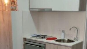 Ett kompakt kök med en inbyggd ugn, en diskho och en liten matplats med ett bord och några pallar.