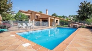 Une piscine avec une terrasse carrelée, un patio couvert et une vue sur une maison dont le toit est en pente.