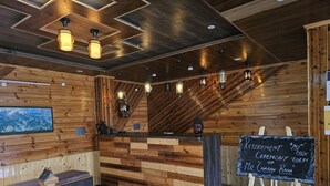 A wooden reception desk with a chalkboard sign for a retirement ceremony, a map on the wall, and a seating area with a glass table. - The Black Morel Hotel & Restaurant (Banjar)
