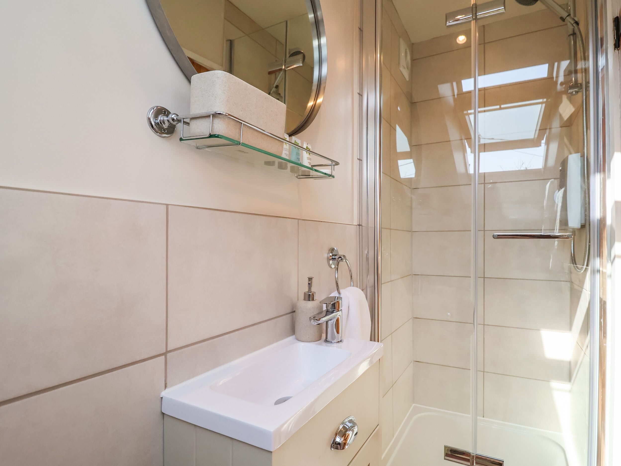 A modern bathroom with a glass shower enclosure, a white sink, and a glass shelf above the sink.