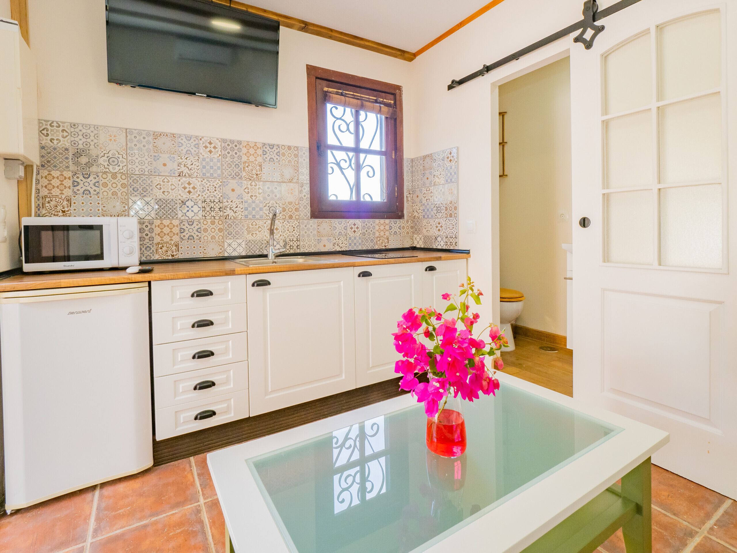 Een keuken met witte kasten, een magnetron, een spoelbak en een raam met decoratieve ijzeren spijlen.