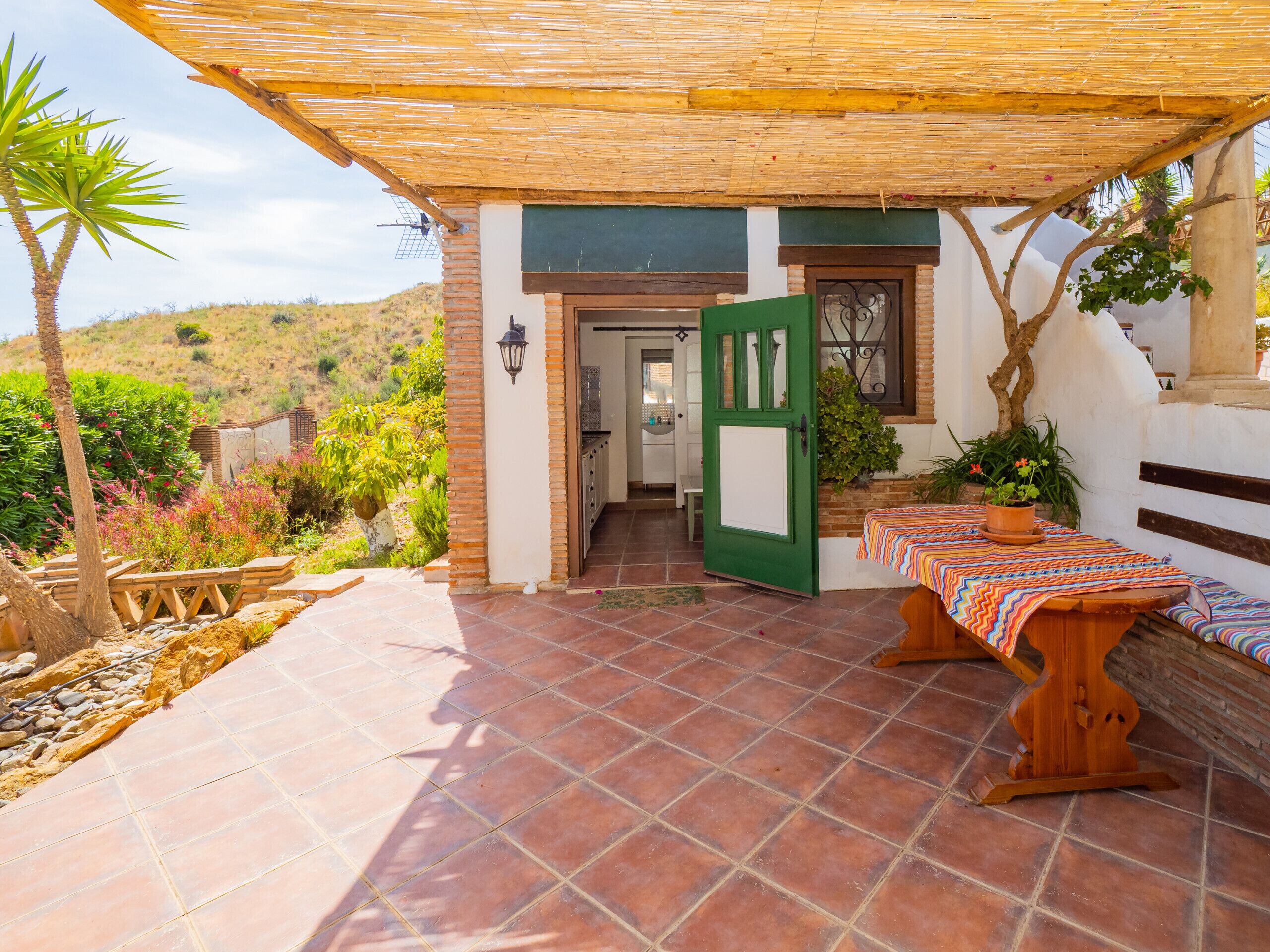 A patio with a wooden table and bench, a green door, and a view of a hillside.