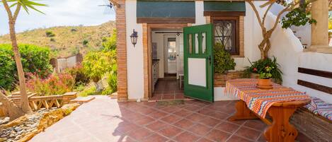 A patio with a wooden table and bench, a green door, and a view of a hillside.