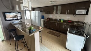 A modern kitchen with dark wooden cabinets, a granite countertop, a built-in microwave, and a gas stove. There is a small island with bar stools and a potted plant. - Pousada Residencial - Atrás Shopping pvh (Porto Velho)