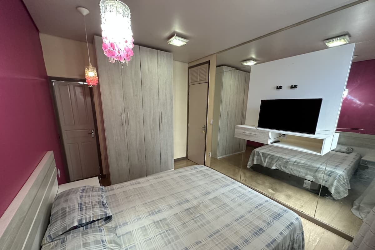 A bedroom with a bed, a TV, a wardrobe, and a mirror.