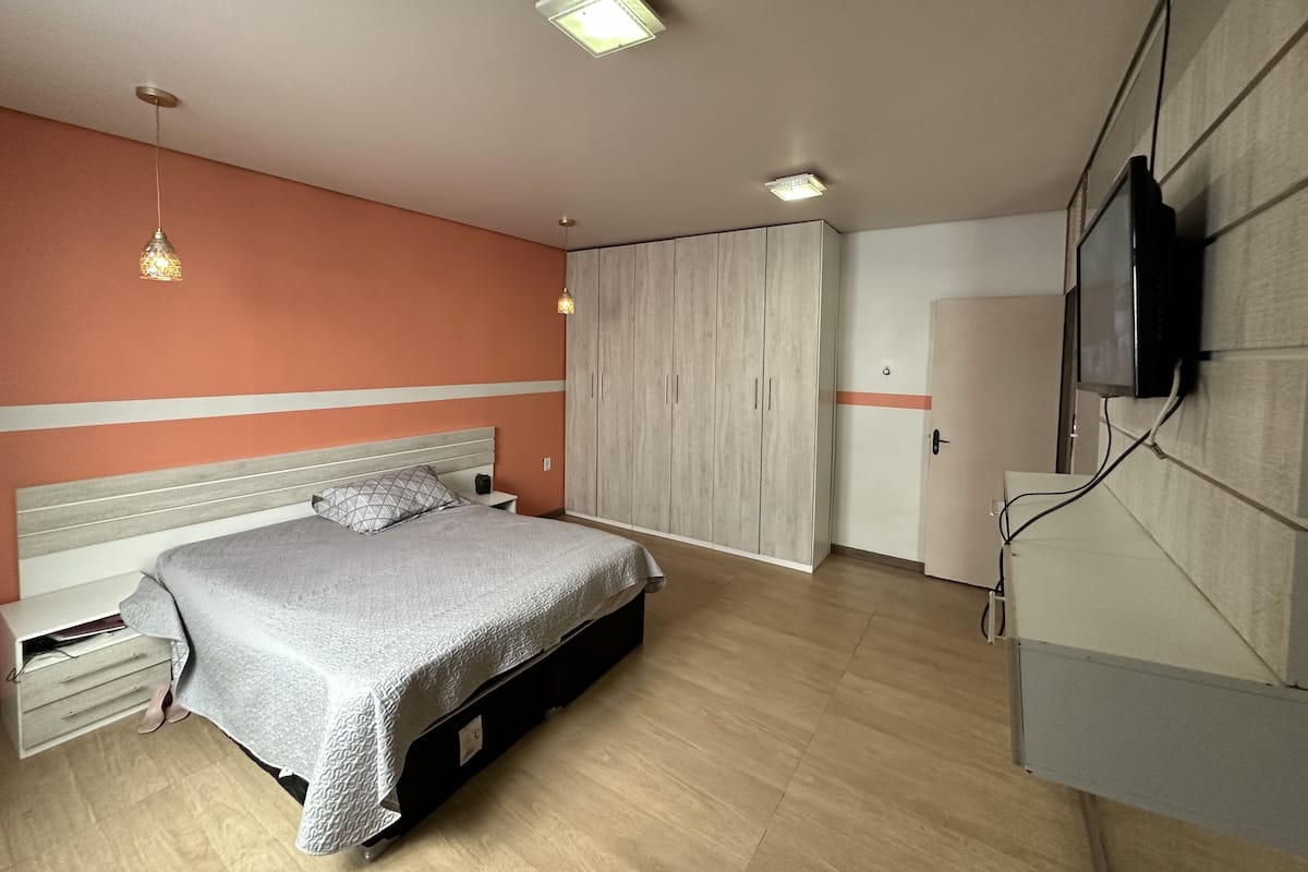 A bedroom with a bed, bedside tables, a wardrobe, a television, and a ceiling light fixture.