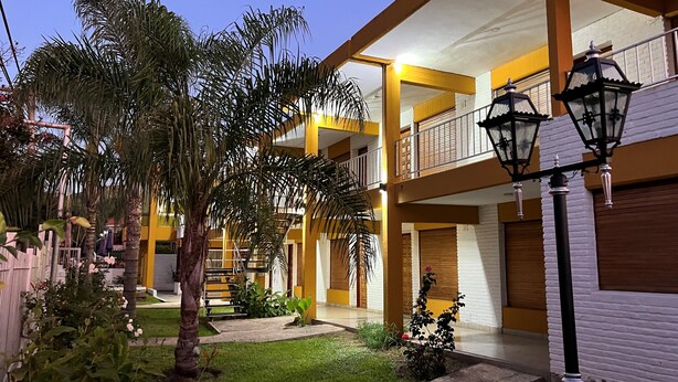 Un edificio de varios pisos con balcones, un jardín con palmeras y un farol.