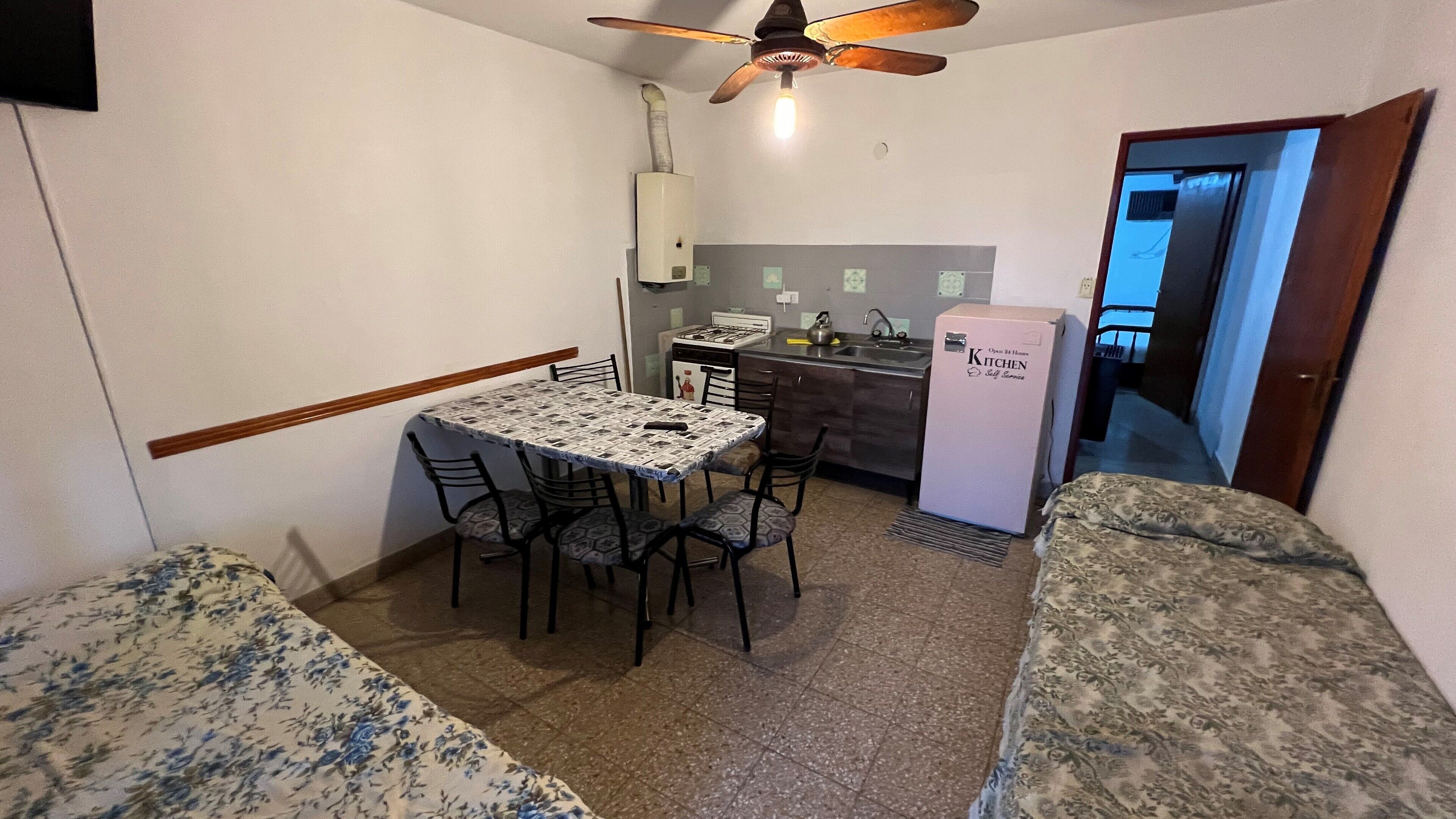 A compact kitchen with a gas stove, sink, and a refrigerator. There is a dining table with chairs and a ceiling fan above.