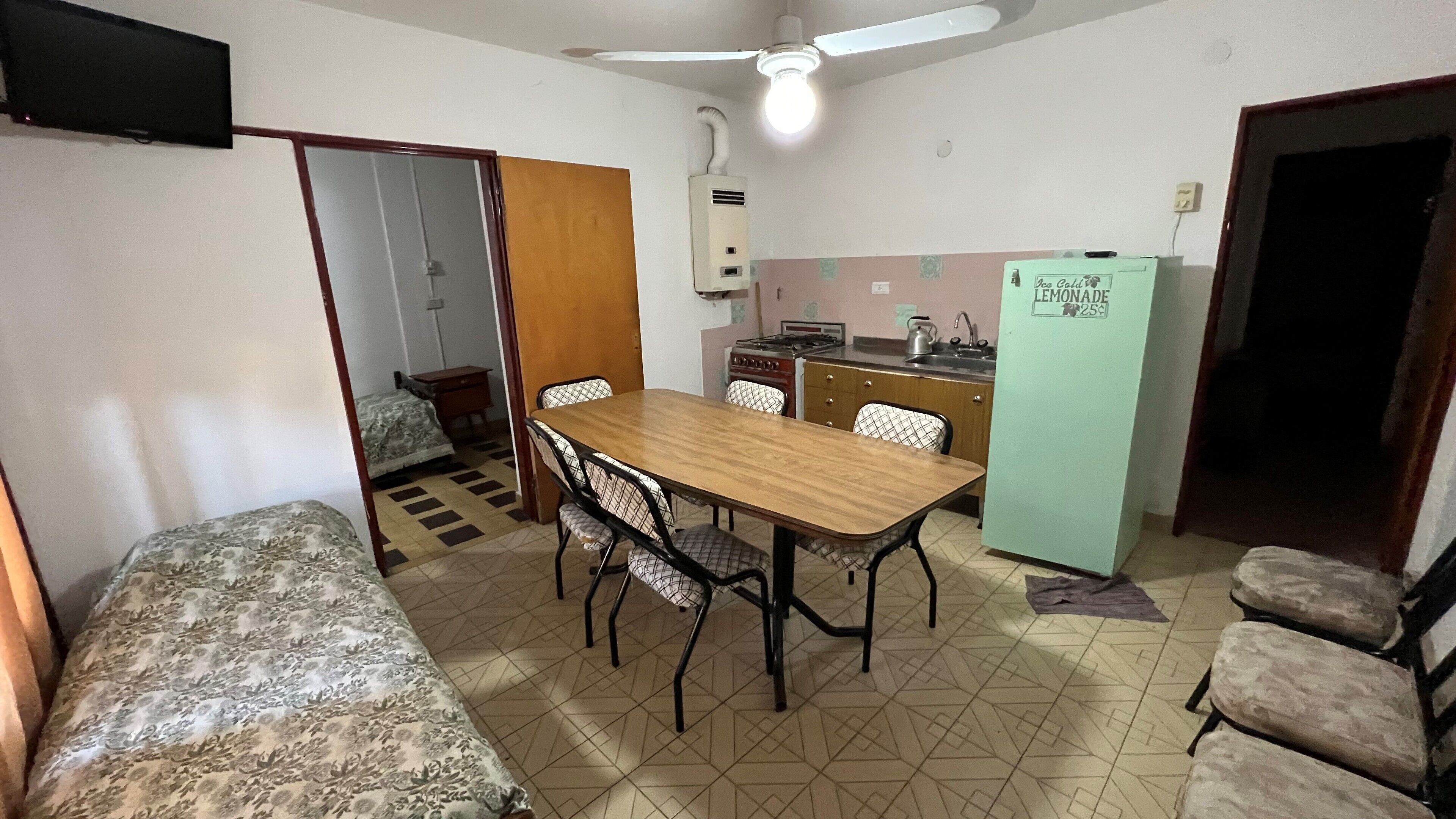 Una habitación compacta con cama, una mesa de comedor con sillas, una kitchenette y un ventilador de techo.