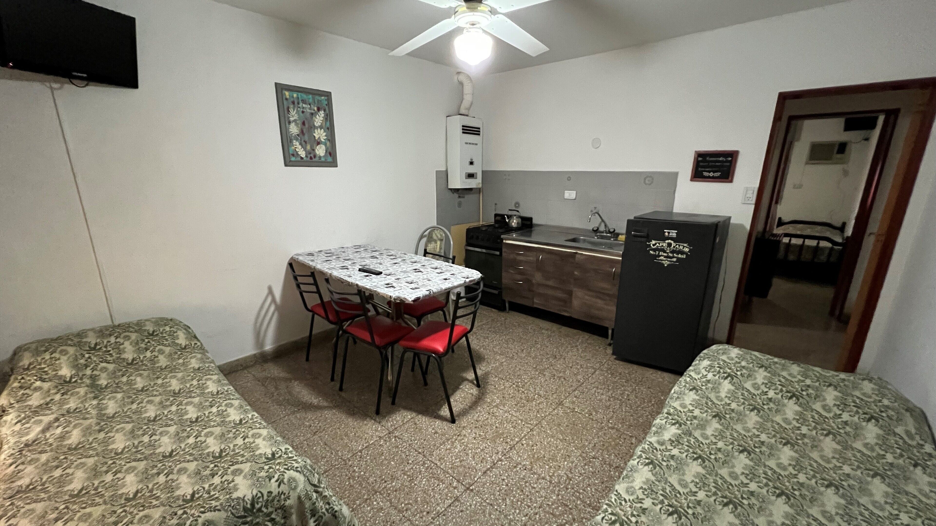 Una habitación compacta con kitchenette, una mesa de comedor con sillas y dos camas con ropa de cama estampada.