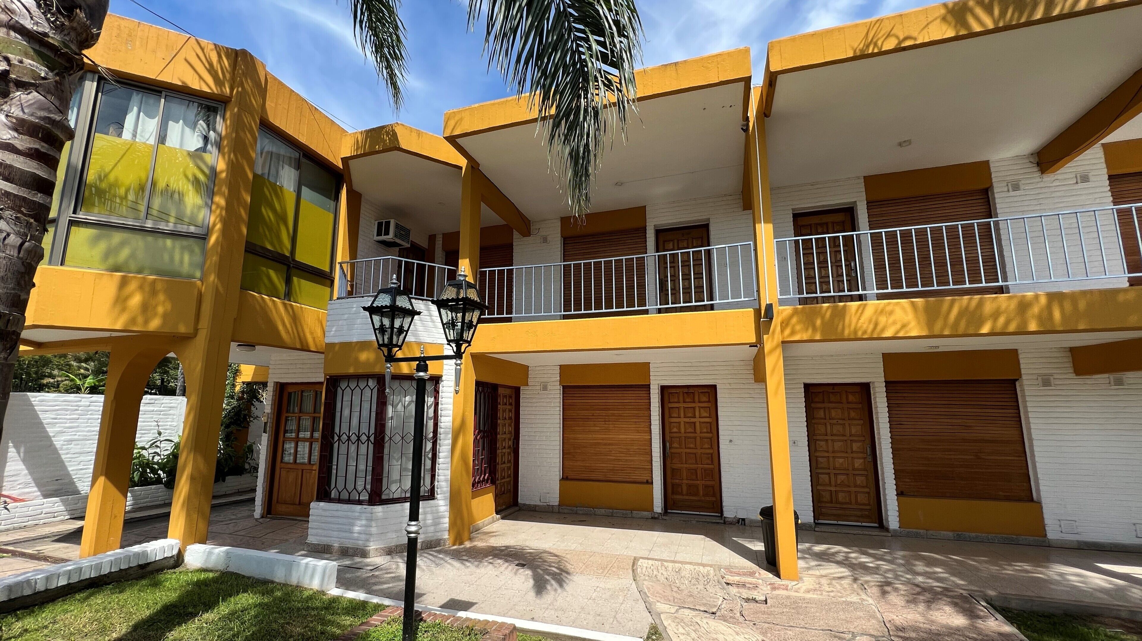 A multi-story building with yellow and white exterior walls, balconies with metal railings, and closed wooden doors.