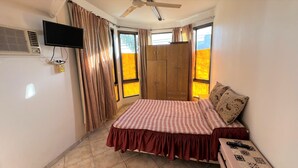 Un dormitorio con cama, cortinas, televisión y ventilador de techo.