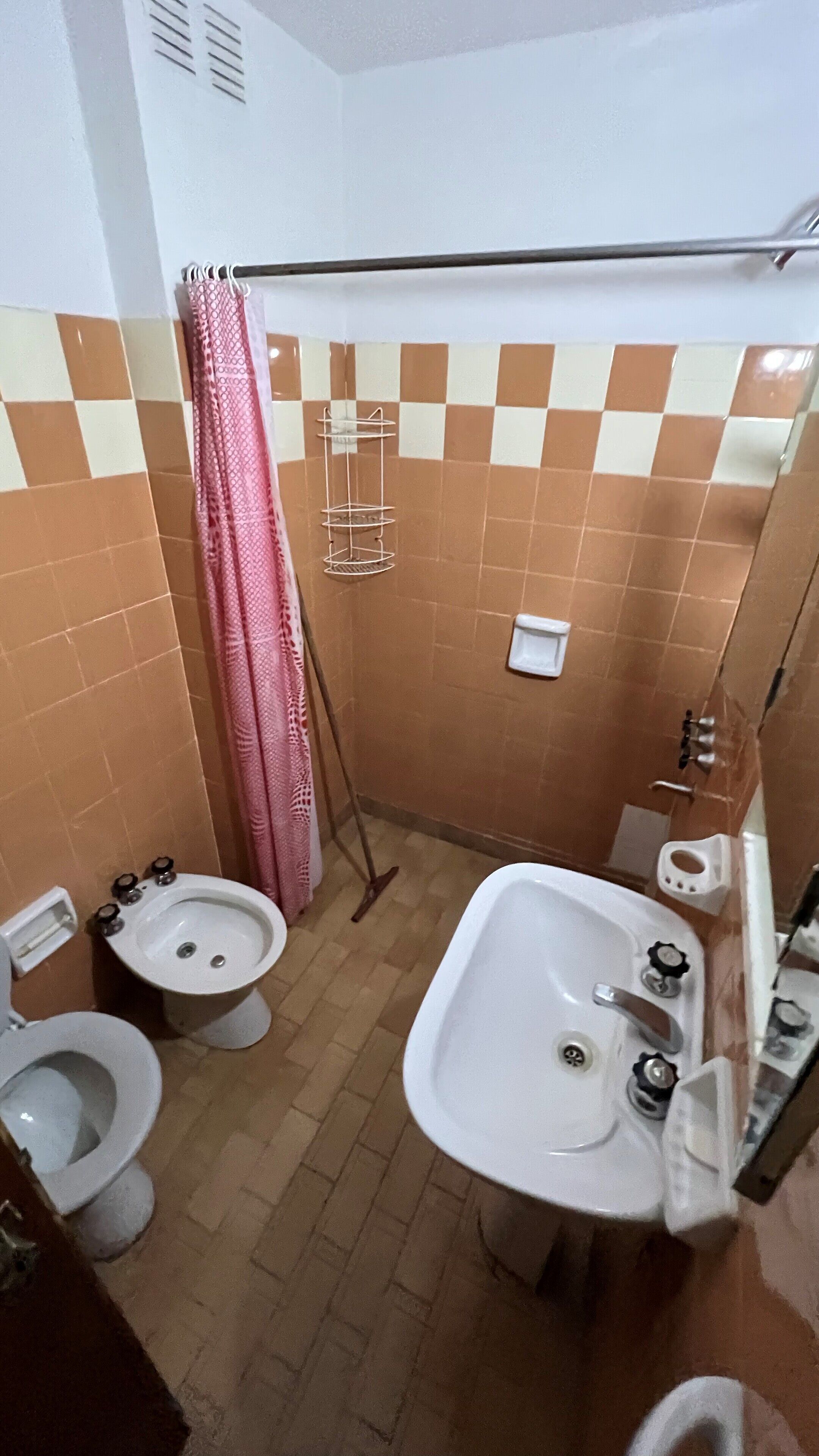 Un baño pequeño con dos inodoros, un lavabo, un bidé y una cortina de ducha.