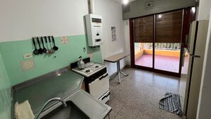 Cocina compacta con estufa a gas, un lavamanos pequeño y una encimera. Se ve una ventana con vistas al exterior.