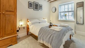 Une chambre avec une armoire en bois, un lit avec du linge de lit blanc, une table de chevet avec une lampe et une fenêtre donnant sur la rue.
