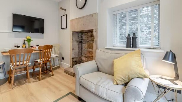 Un salon comprenant un canapé, une table à manger avec des chaises, une cheminée, un téléviseur fixé au mur et une fenêtre avec des stores.
