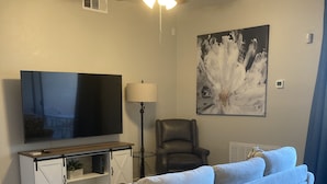 Un salon avec un canapé, un téléviseur, un ventilateur de plafond et des œuvres d’art accrochées au mur.