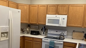 Une cuisine moderne avec des meubles en bois, un réfrigérateur blanc, un four à micro-ondes et une cuisinière à gaz.