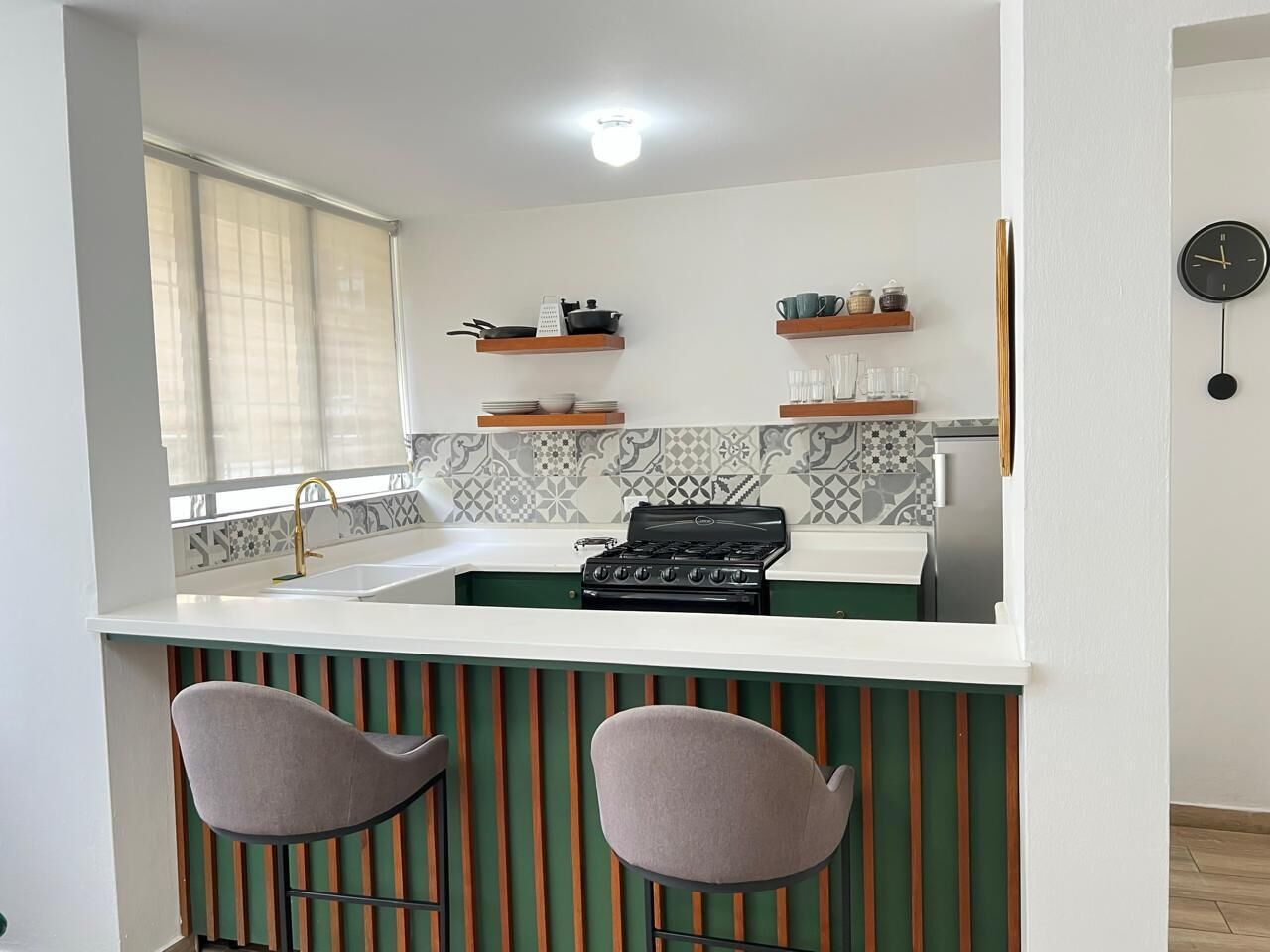 Cozinha compacta com fogão a gás, dois banquetes altos e janela com cortinas finas.