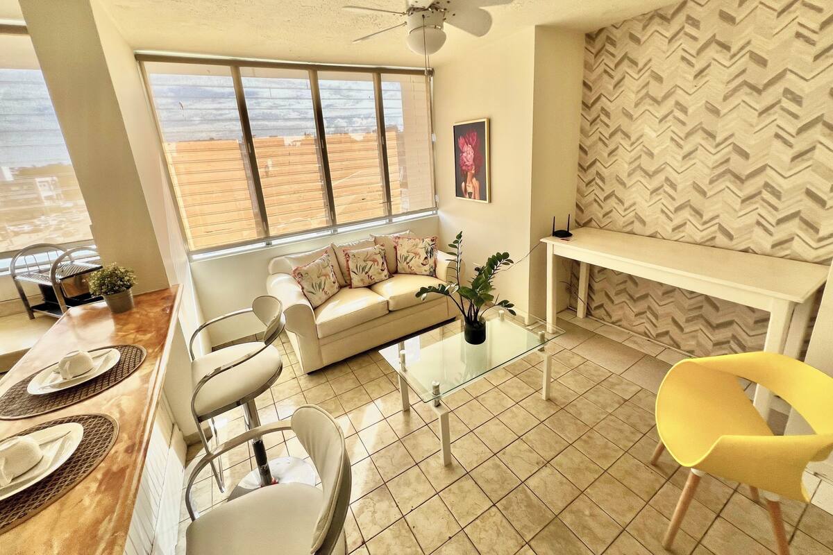A living room with a sofa, chairs, a coffee table, a TV, and a large window with a view.