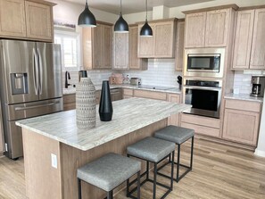 A modern kitchen with wooden cabinets, stainless steel appliances, a marble countertop, and bar stools. - Brand new luxury townhome in the heart of Ruidoso! (Ruidoso)