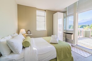 A hotel room with a bed, a nightstand with a lamp, and a view of the outdoors. - Elevate Vacation Alpenglow Lodge - Sunset Boulevard #504 (Whistler)