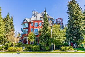 A multi-story building with a red and grey facade, large windows, and a balcony. - Elevate Vacation Alpenglow Lodge - Sunset Boulevard #504 (Whistler)