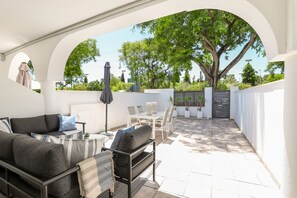 Een terras buiten met een bank, eettafel, stoelen en een overdekt gedeelte.