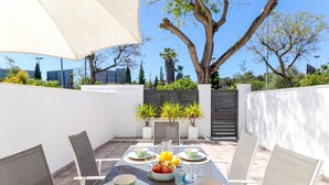 An outdoor dining area with a table set for four, surrounded by chairs, and a large umbrella providing shade. - Superb townhouse with big sunny terrace (Marbella)