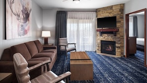 Une chambre d’hôtel moderne avec une cheminée en pierre, un canapé, une table basse en bois et un téléviseur fixé au mur.