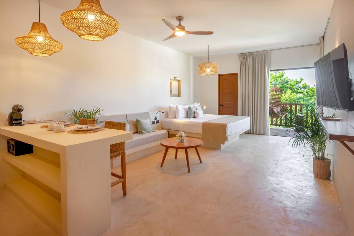 Une chambre d’hôtel moderne équipée d’un canapé, d’une petite table à manger, d’un ventilateur de plafond et d’un balcon avec un téléviseur.