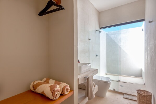 Un baño moderno con cabina de ducha de cristal, repisa de madera con toallas y lavamanos blanco.