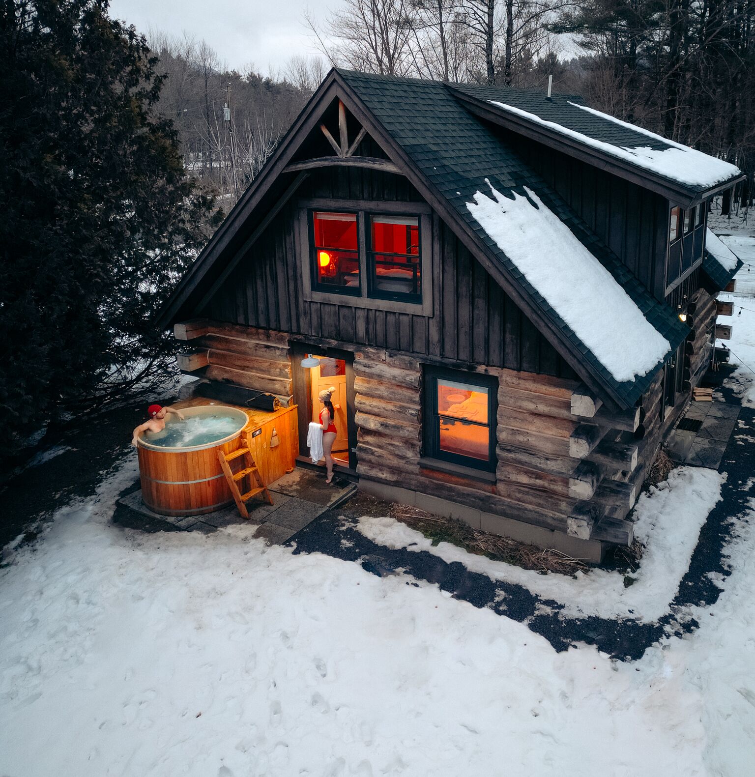 Une cabane en rondins avec un jacuzzi et une cheminée visible à travers les fenêtres.