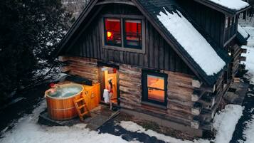 Une cabane en rondins avec un jacuzzi et une cheminée visible à travers les fenêtres.