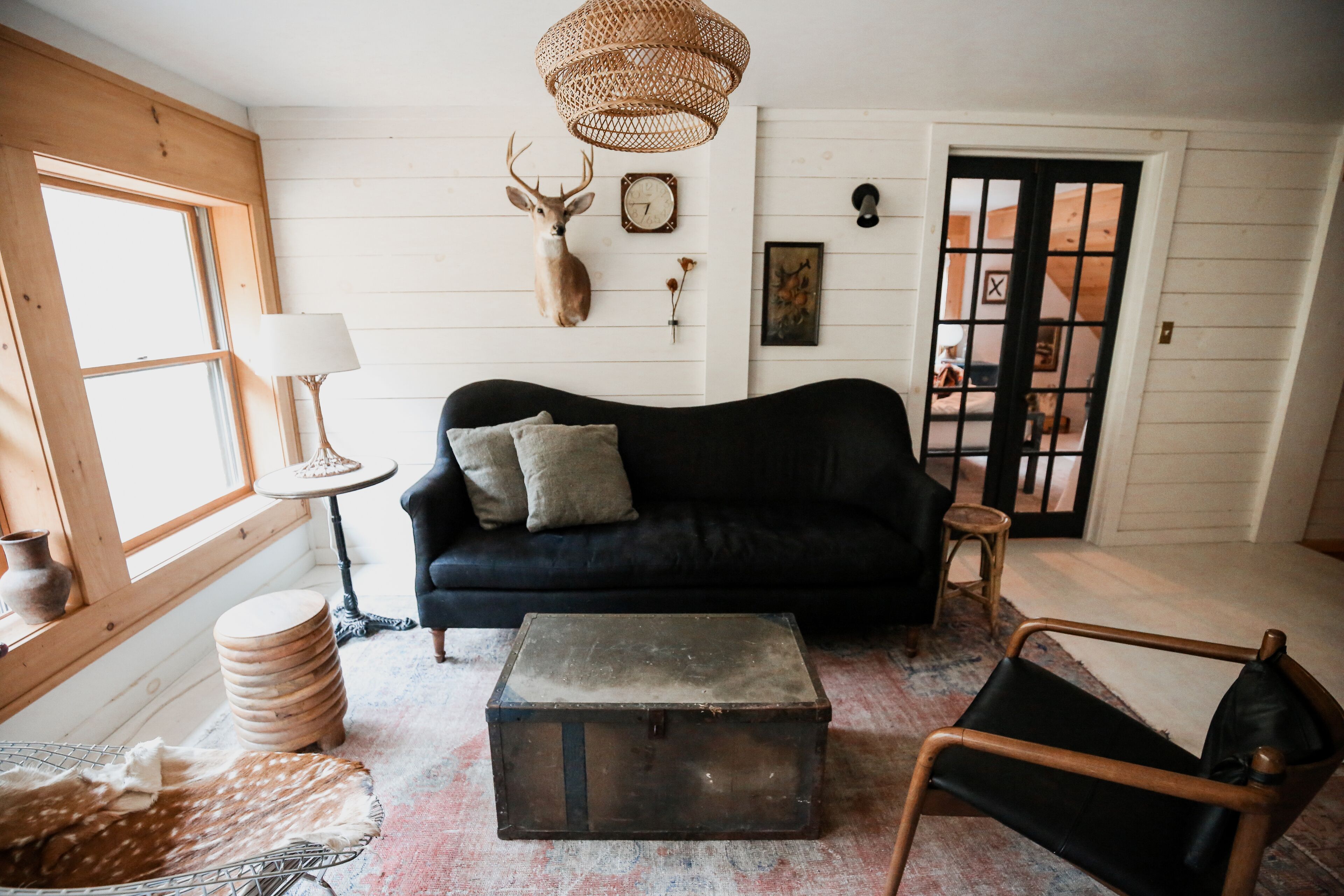 A cozy living room with a black sofa, a wooden chest, and a woven light fixture.