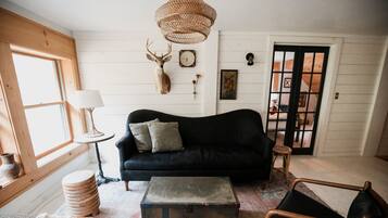 A cozy living room with a black sofa, a wooden chest, and a woven light fixture.