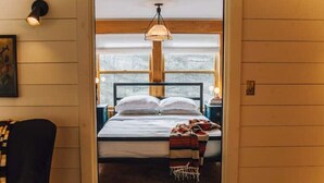 Ein gemütliches Schlafzimmer mit Bett, Nachttisch, Lampe und Fenster mit Blick.