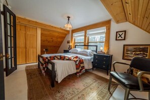 Une chambre à coucher avec un lit, une table de chevet, une chaise, un plafond en bois et une fenêtre.
