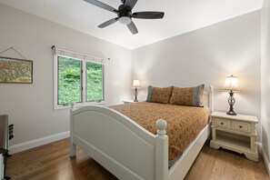 A bedroom with a white bed, two bedside tables with lamps, a ceiling fan, and a window with blinds. - Cozy wooded mountain retreat 10 minutes from downtown Asheville (Asheville)