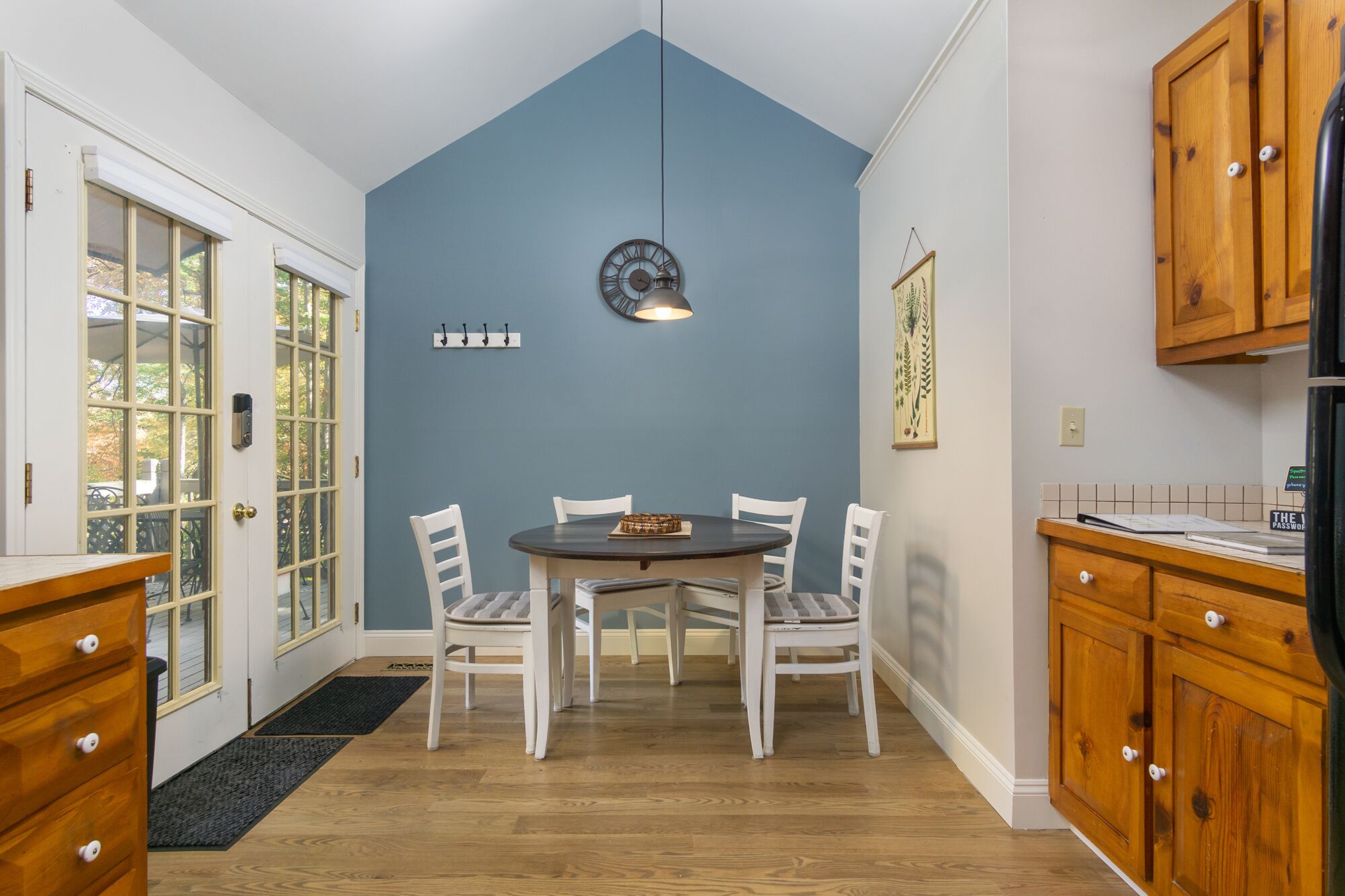 A dining area with a round table and four chairs, a clock on the wall, and wooden cabinets.