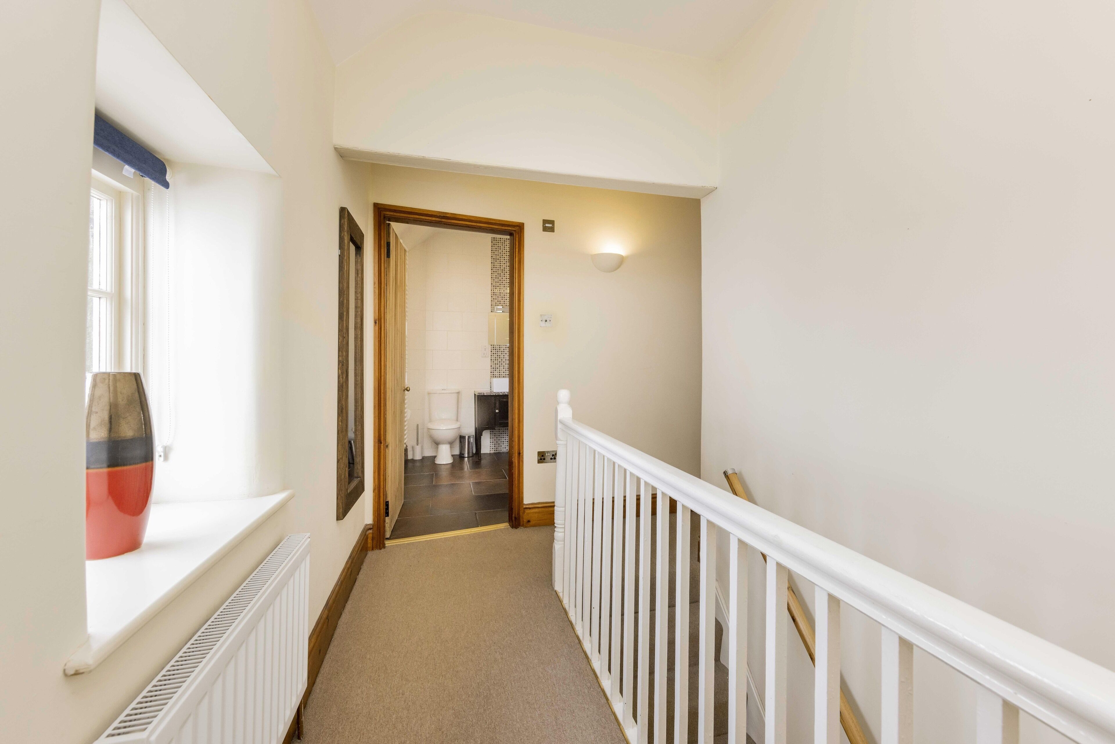 A hallway with a white railing, a radiator, and a window with a vase.