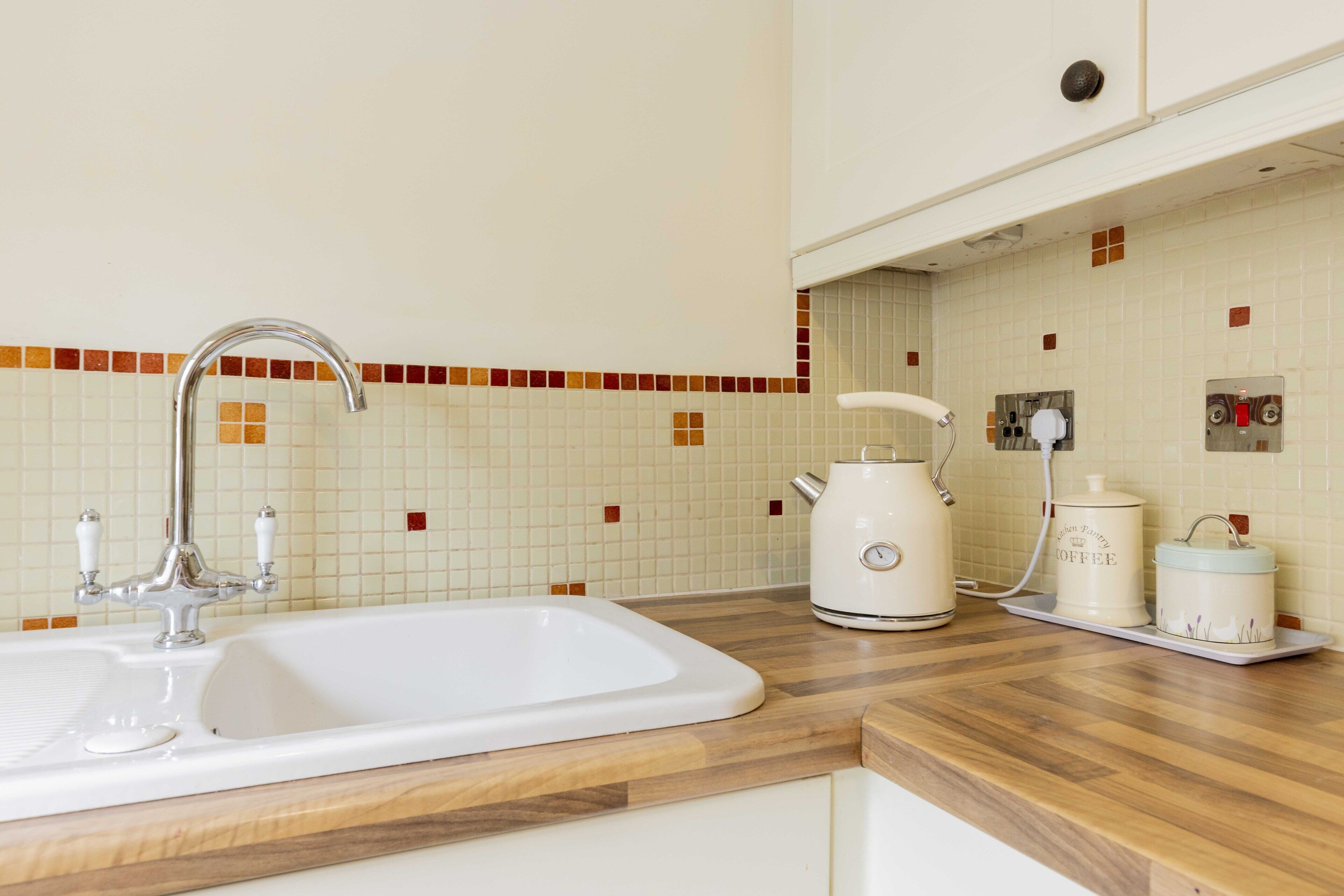A kitchen with a white sink, a coffee maker, and a kettle on the counter.