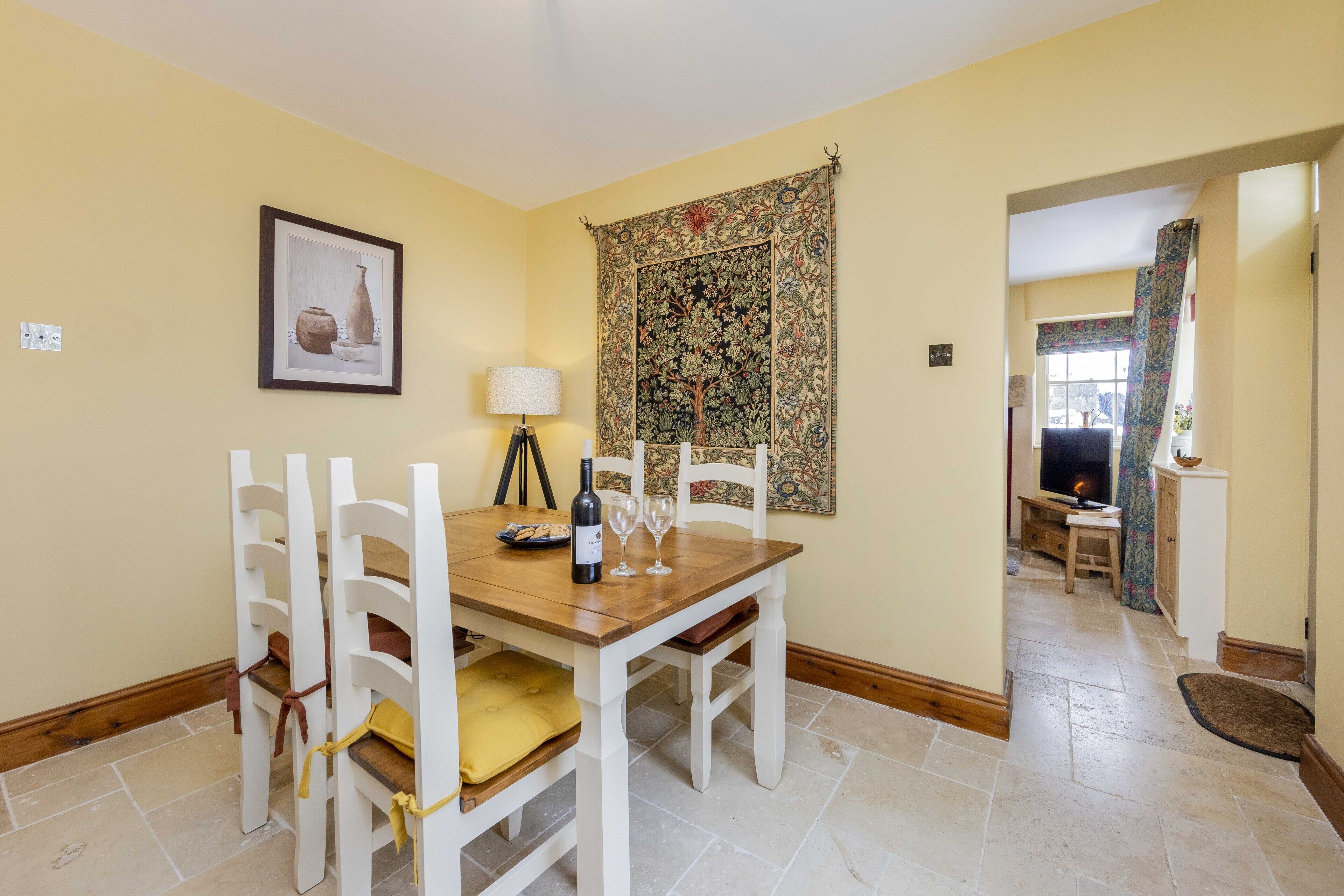A dining area with a wooden table and white chairs, a wine bottle, and two wine glasses.