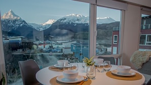 Ein Essbereich mit Blick auf die Berge, ein Tisch gedeckt mit weißen Tellern und Schüsseln sowie moderne Stühle.