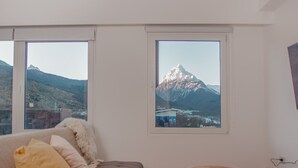 Ein modernes Wohnzimmer mit einer Couch, zwei Fenstern mit Bergblick und einer Holzbalkendecke.